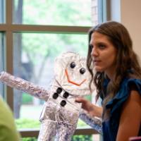 Teacher engages with attendees, holding a tinfoil gingerbread man at student project showcase